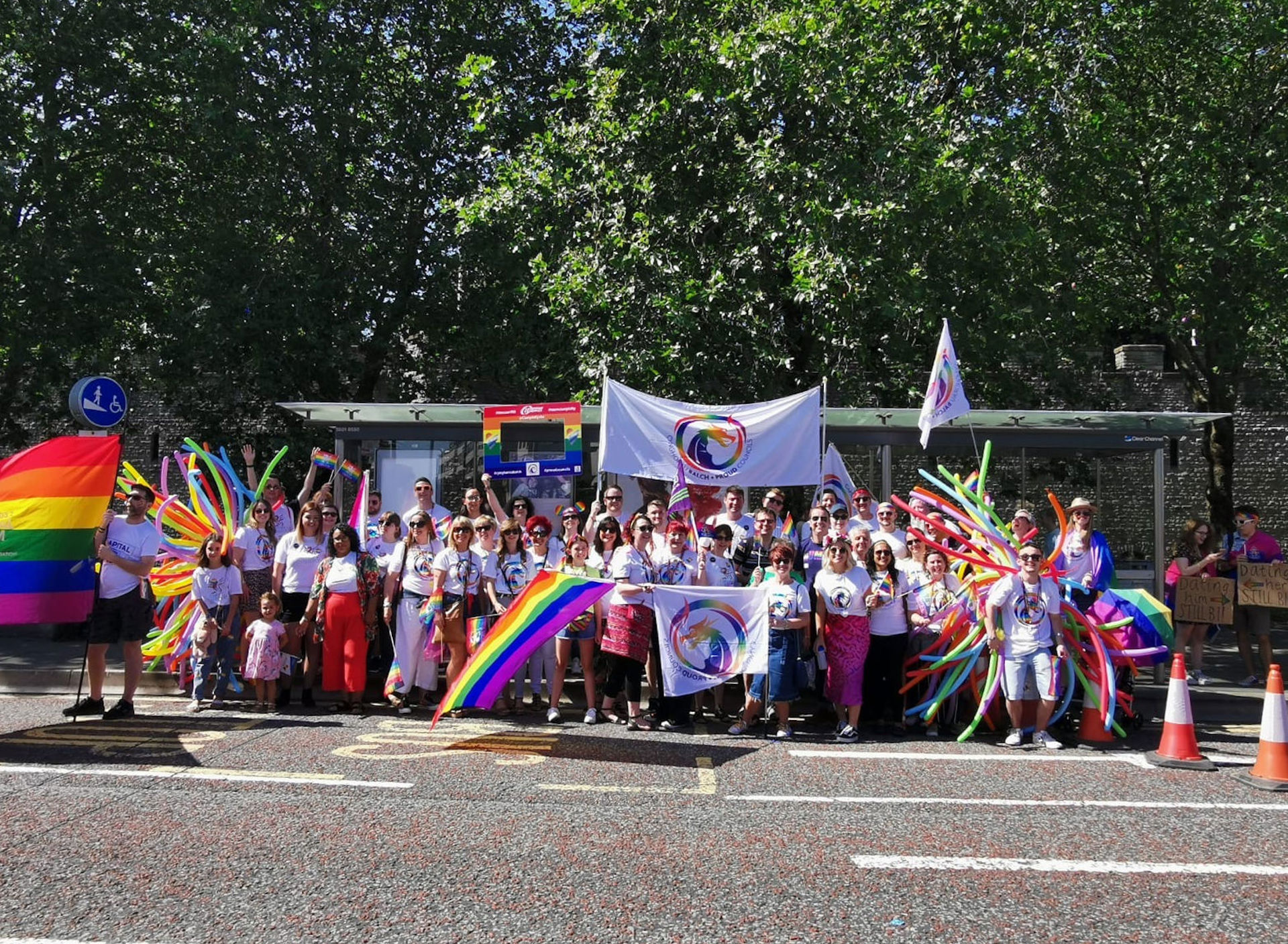 A crowd waves rainbow-coloured flags and balloons in support of LGBTQ+ pride, with some of the rainbow flags showing the insignia of ‘Proud Councils’.