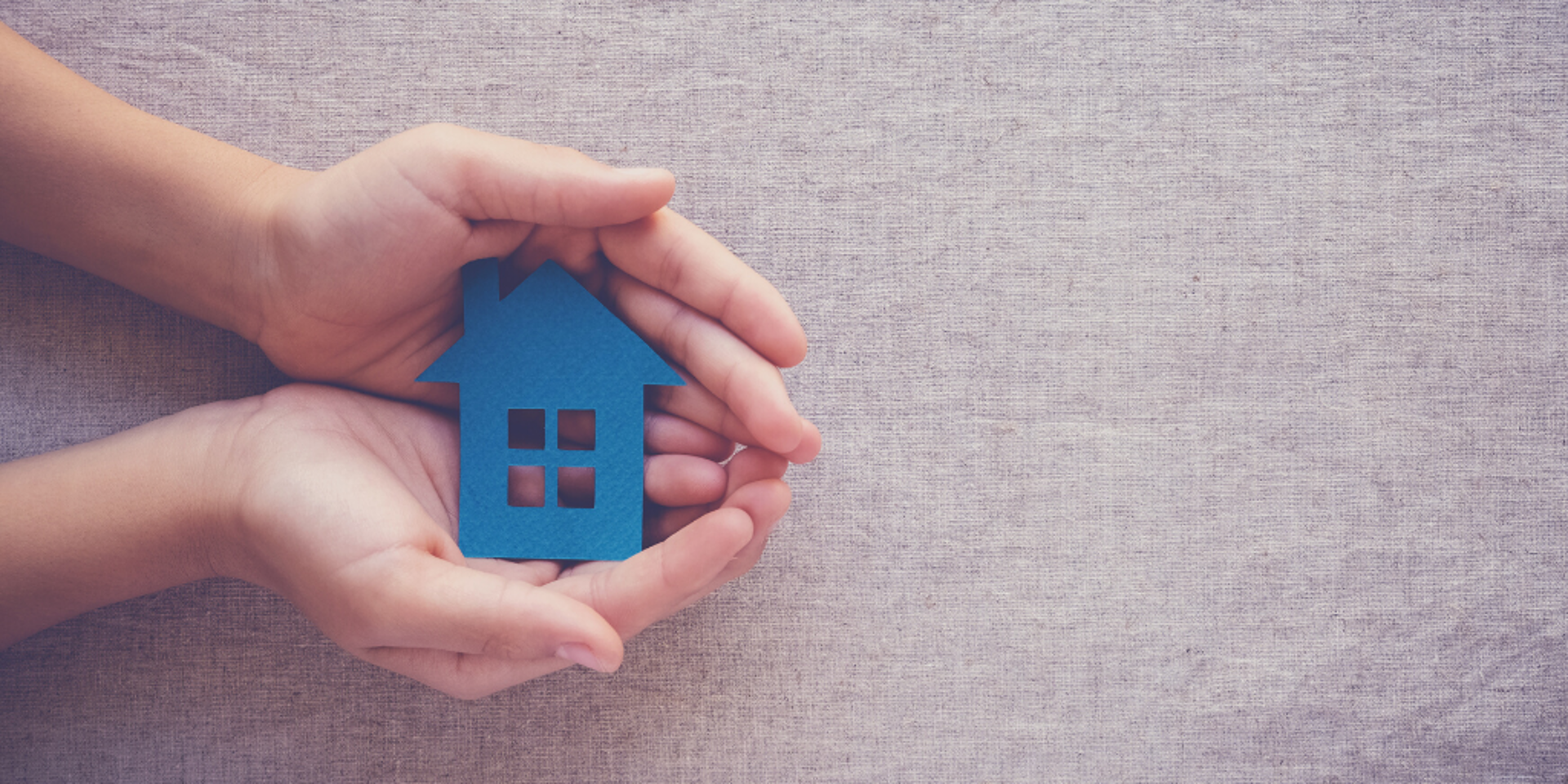 A small blue paper house in the palm of two hands.