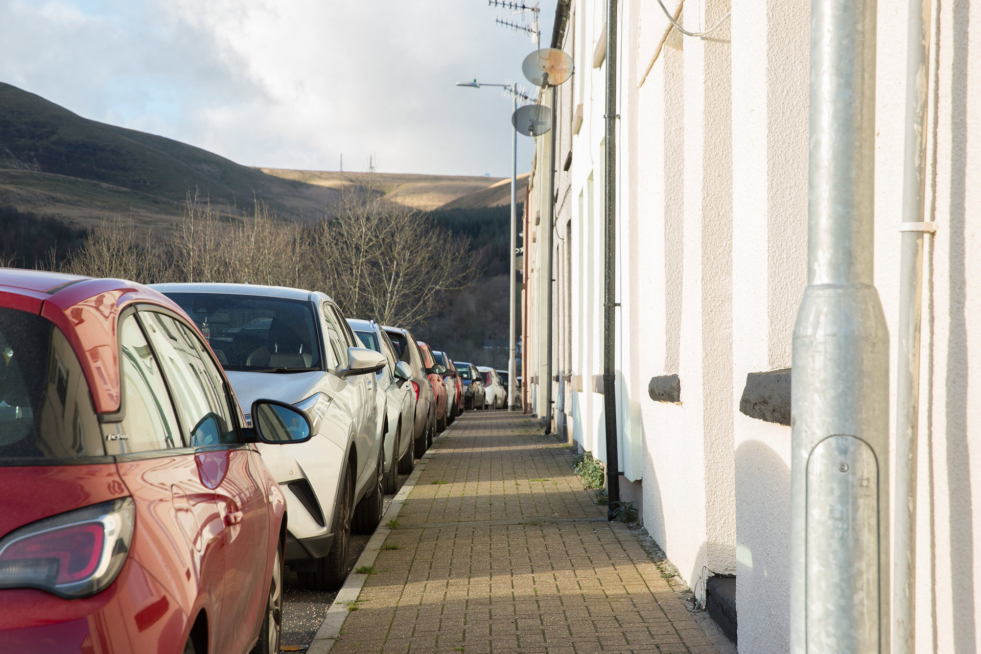 A line of cars parked next to terraced housing.